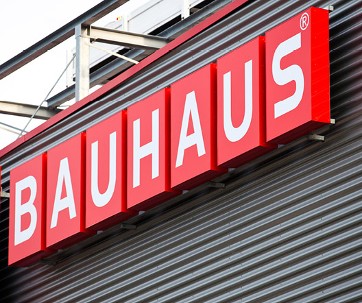 BAUHAUS-Schriftzug in Rot an der Fassade eines Gebäudes, klar erkennbar vor einer strukturierten Metallverkleidung.