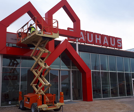 Installation der BAUHAUS-Leuchtreklame an der Fassade mit Hebebühne, Monteure in Aktion.