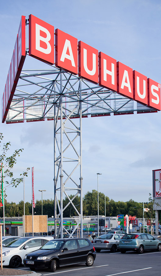 Große BAUHAUS-Leuchtreklame auf einer hohen Stahlkonstruktion, sichtbar über einem Parkplatz.