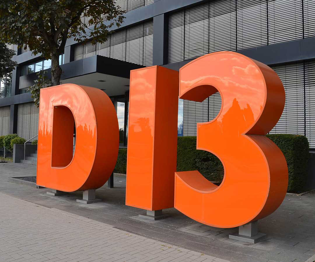 Seitenansicht des orangefarbenen „D 13“-Schriftzuges in Einzelbuchstaben.