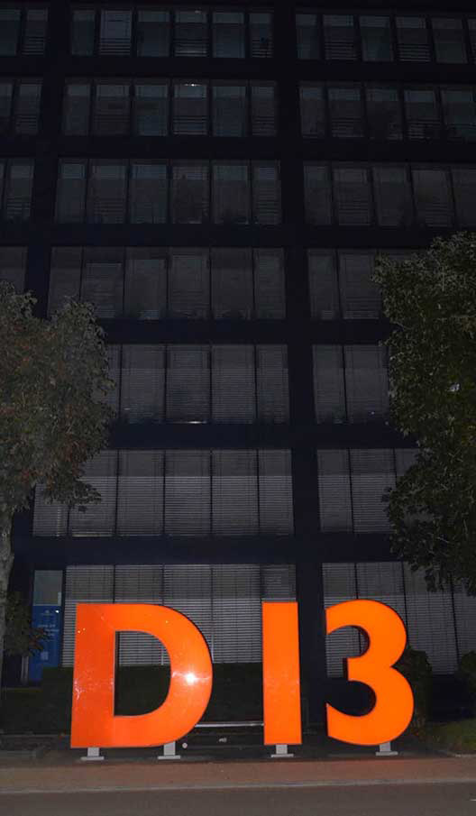 Orangefarbener „D 13“-Schriftzug bei Nacht vor einem modernen Firmengebäude.