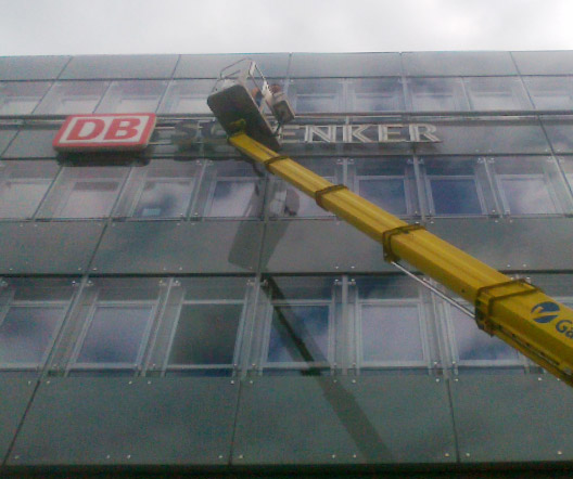 Montage der DB Schenker-Leuchtschrift an einer Glasfassade mit einem Hubwagen.