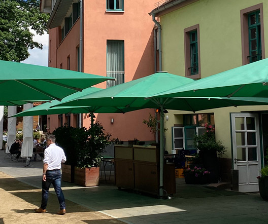 Eingangsbereich der Gerbermühle in Frankfurt mit grünen Sonnenschirmen und einem Mann, der den Hof betritt.