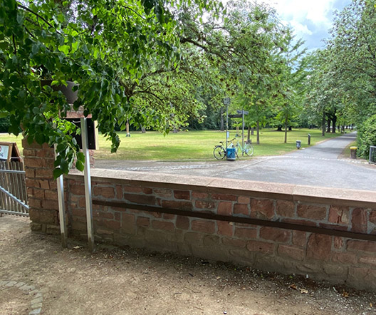 Blick auf einen ruhigen Parkbereich hinter der Steinmauer bei der Gerbermühle in Frankfurt.