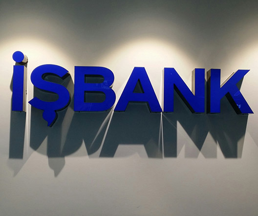 Leuchtendes IŞBANK-Logo an der Innenwand einer Filiale, das Schatten auf die dahinterliegende Fläche wirft.