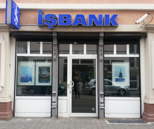 Frontalansicht eines Eingangs einer IŞBANK-Filiale in einem historischen Gebäude mit großen Glasfenstern.