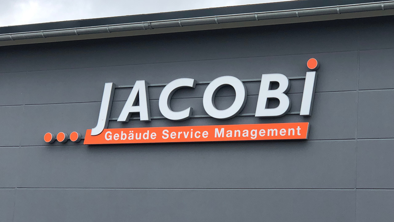 Schriftzug „Jacobi Gebäude Service Management“ an der Fassade eines Gebäudes.