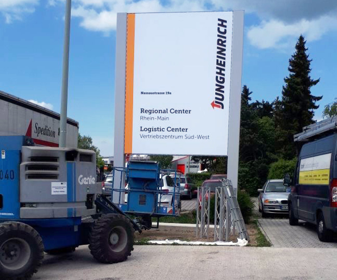 Werbetafel für das Jungheinrich Regional Center auf einem Parkplatz mit Hebebühne der Installateure.