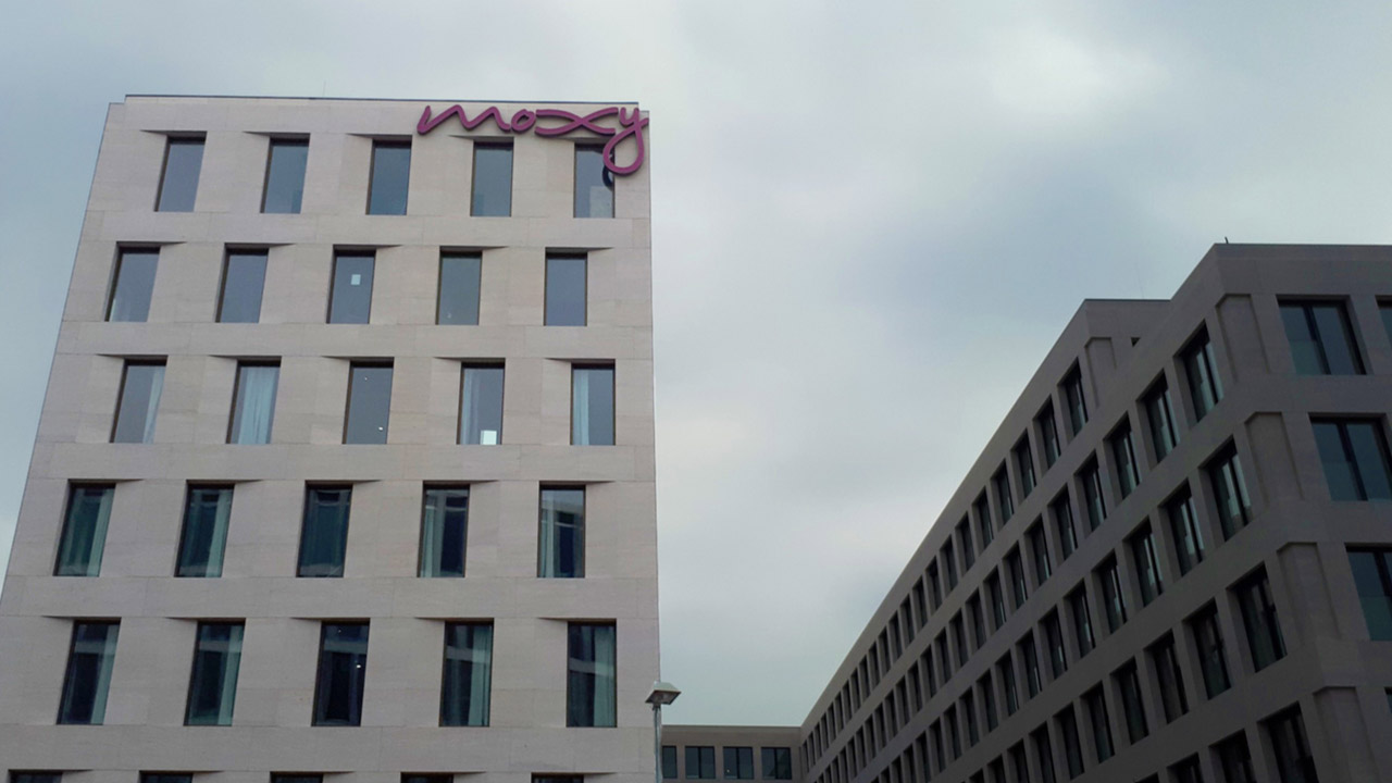 Moxy Hotels Leuchtschrift auf dem Dach eines modernen Gebäudes in Darmstadt, gut sichtbar gegen den grauen Himmel.