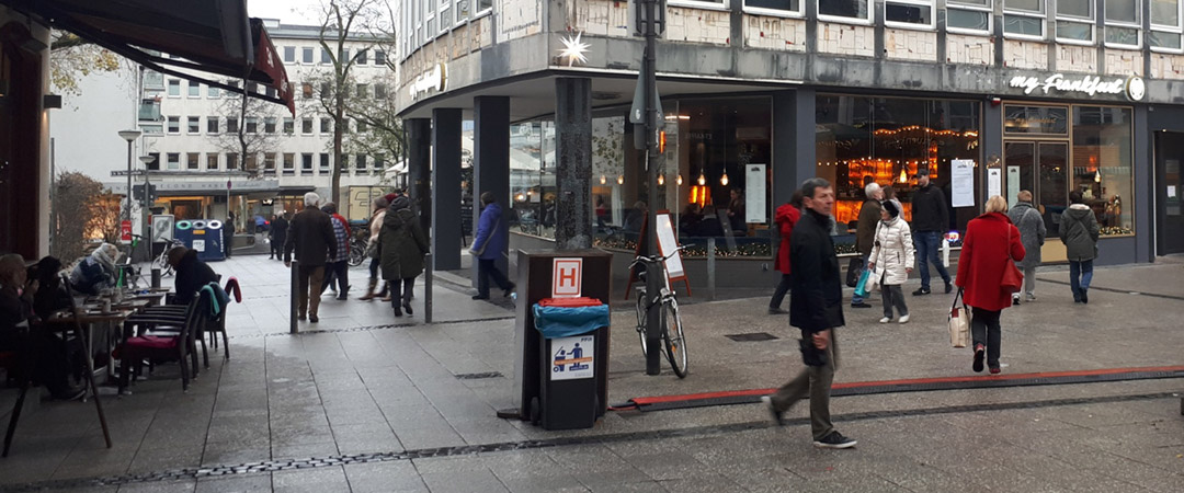 Straßenszene vor dem „My Frankfurt“ Café, Menschen gehen vorbei und einige Gäste sitzen im Außenbereich.