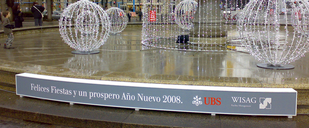 Spanischer Neujahrsgruß von UBS und WISAG auf einem beleuchteten Schild vor dem festlich beleuchteten Brunnen vor der Alten Oper in Frankfurt.