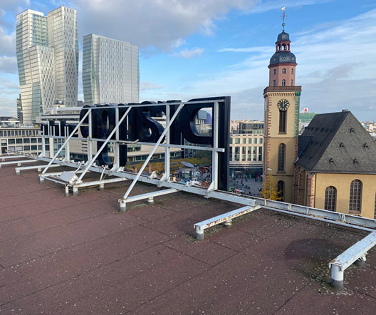 Rückseite der Dachkonstruktion für die Leuchtschrift „Prange Schuhe“ mit Blick auf die Frankfurter Skyline.