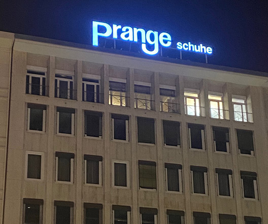 Nachtansicht der Leuchtschrift „Prange Schuhe“ auf dem Dach eines Gebäudes in Frankfurt.