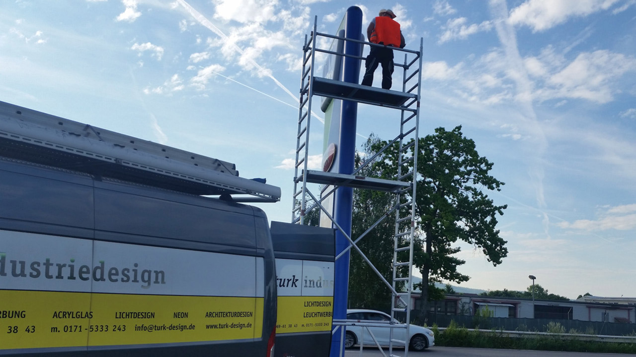 Monteur auf einem Gerüst, das an einem OMV-Tankstellen-Pylons steht